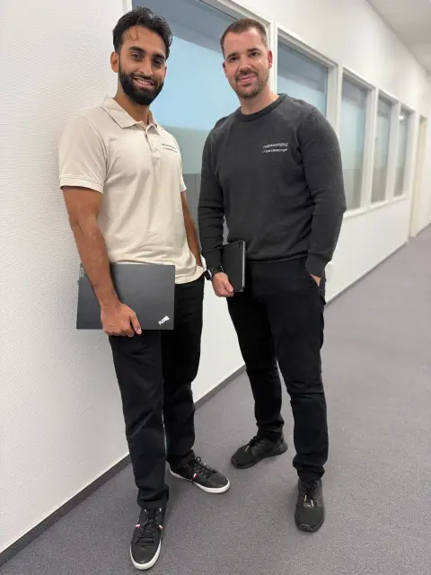 Zwei Mitarbeiter von netzwerkfähig stehen mit Notebooks im Büroflur vor einer Fensterfront