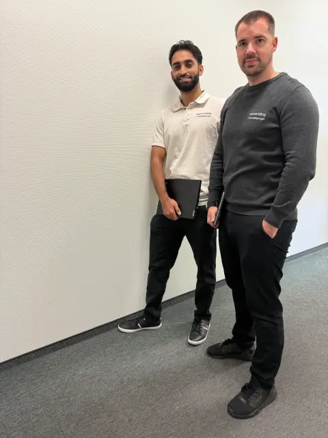 Zwei Mitarbeiter von netzwerkfähig stehen entspannt mit Notebooks im Flur