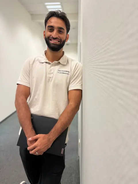 Mitarbeiter von netzwerkfähig lehnt mit Notebook im Türrahmen zum Büroflur