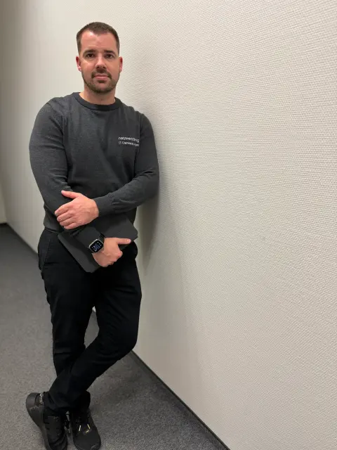 Mitarbeiter von netzwerkfähig lehnt mit Notebook an der Wand im Büroflur
