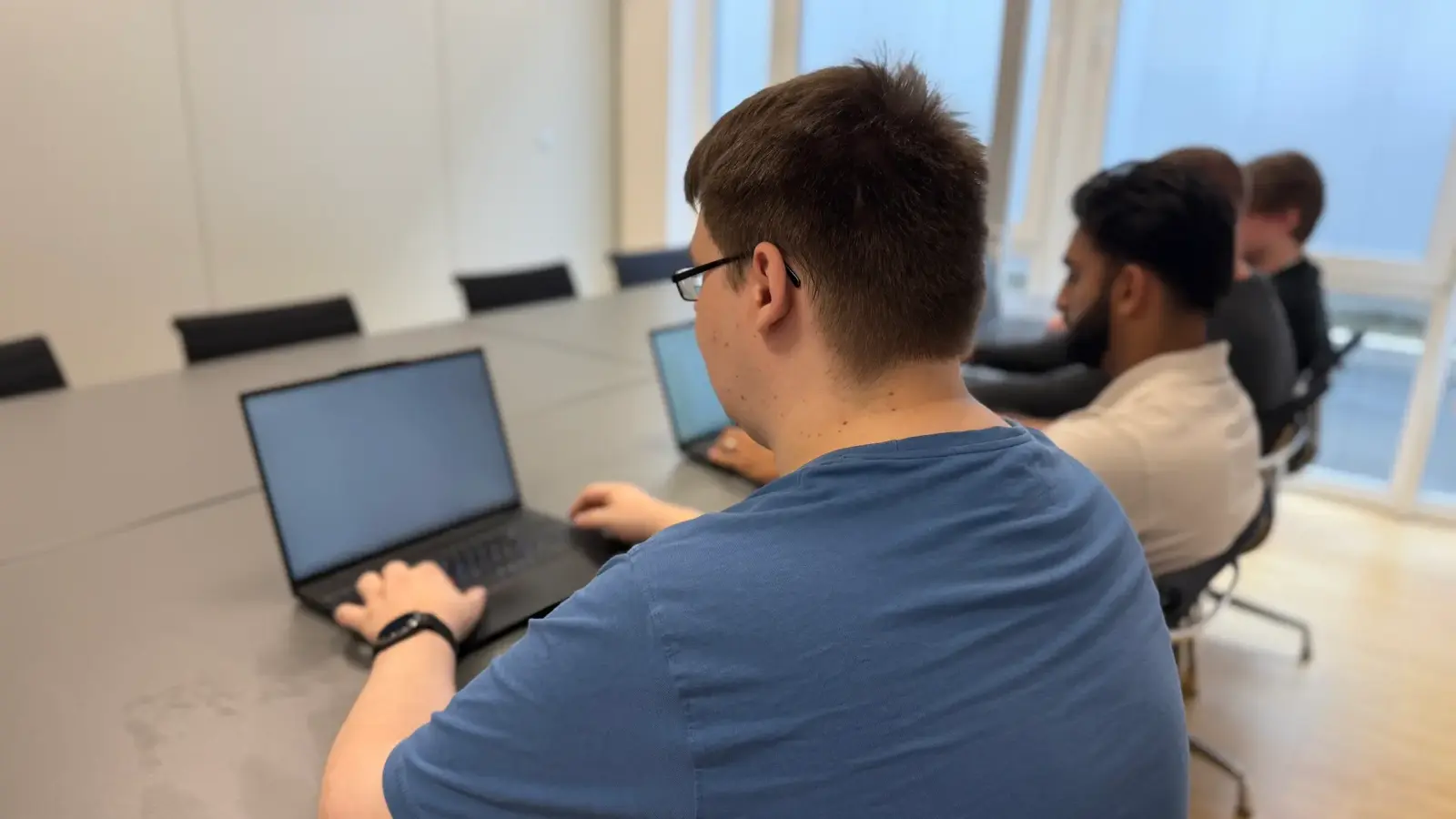 Mitarbeiter von netzwerkfähig am Notebook, dahinter Kollegen im Besprechungsraum