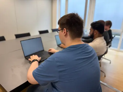 Mitarbeiter von netzwerkfähig am Notebook, dahinter Kollegen im Besprechungsraum