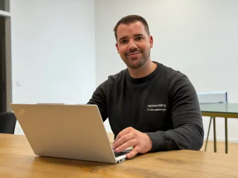 Mitarbeiter von netzwerkfähig arbeitet lächelnd am Notebook