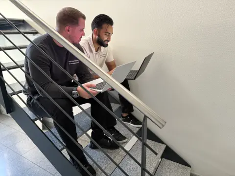 Zwei Mitarbeiter besprechen sich mit Notebooks auf der Treppe