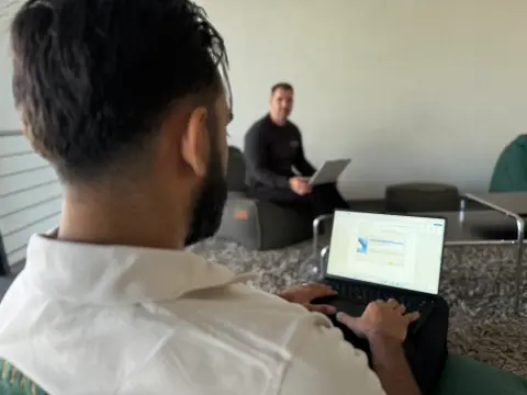 Mitarbeiter arbeitet am Notebook in der Lounge, Kollegen im Hintergrund