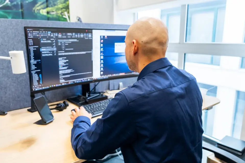 Mitarbeiter von netzwerkfähig am Schreibtisch vor einem großen Monitor mit Konsolenfenster und Windows-Desktop