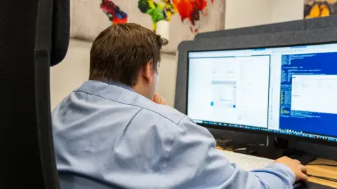 Mitarbeiter von netzwerkfähig am Arbeitsplatz vor zwei Monitoren mit Systemansichten