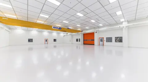 Leere Industriehalle mit spiegelnder heller Bodenbeschichtung, Hallenkran und orangefarbenem Schnelllauftor