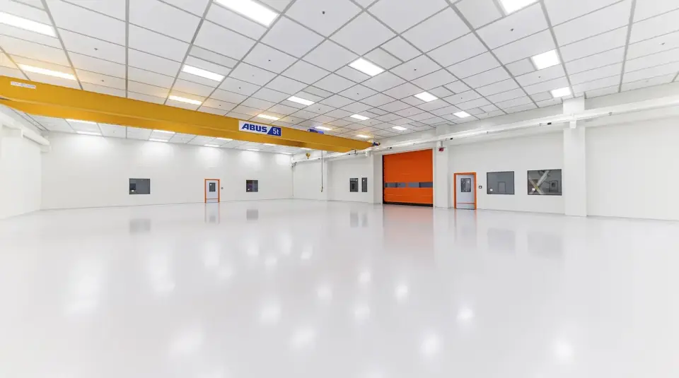 Leere Industriehalle mit spiegelnder heller Bodenbeschichtung, Hallenkran und orangefarbenem Schnelllauftor
